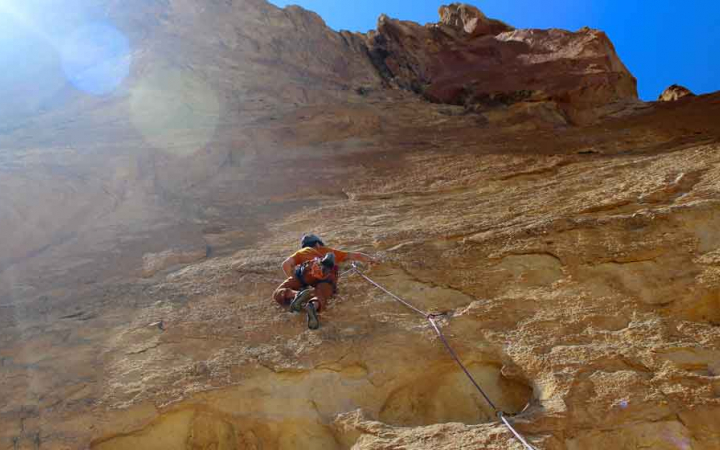 a person navigates a climbing route with blue sky above